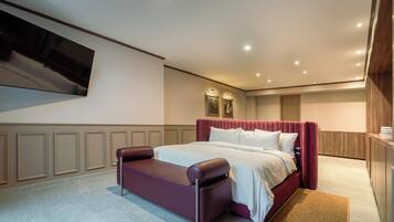 Quarto de hotel com uma cama grande, área de estar, televisão de tela plana na parede e design de painéis de madeira nas paredes.