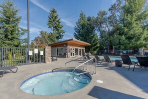 A pool area with a hot tub, lounge chairs, and a small building, surrounded by trees.