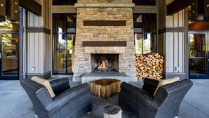 A stone fireplace with a log fire, surrounded by wicker furniture and a wooden stool. - Seaside 2 bdrm Townhome (Parksville)