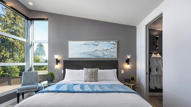 Une chambre moderne avec un grand lit, une vue sur l’extérieur et un tableau accroché au mur.