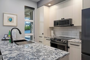 A modern kitchen with a marble countertop, stainless steel appliances, and a view through a glass door.