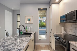 A modern kitchen with a marble countertop, stainless steel appliances, and a window providing a view of the outdoors.