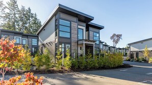 Un immeuble résidentiel moderne à plusieurs étages, doté d’un toit plat, de grandes fenêtres et d’un jardin paysager à l’avant.