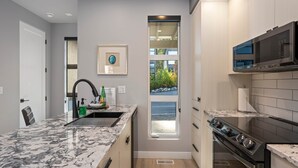 A kitchen with a granite countertop, stainless steel appliances, a window with a view, and a framed picture on the wall. - Seaside 2 bdrm Townhome (Parksville)