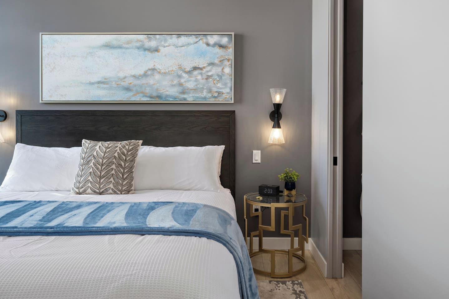 Een slaapkamer met een bed, een nachtkastje, een wandklok en een schilderij.