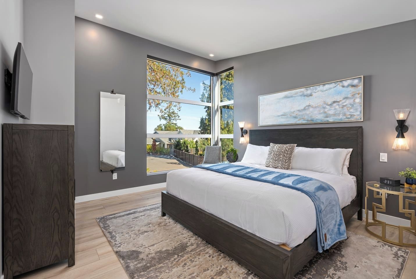 Ein modernes Schlafzimmer mit einem großen Bett, Blick durch ein Fenster und einem Gemälde an der Wand.
