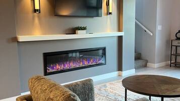 Una sala de estar moderna con un televisor de pantalla plana sobre la chimenea, un sofá cómodo y una mesa de centro redonda.
