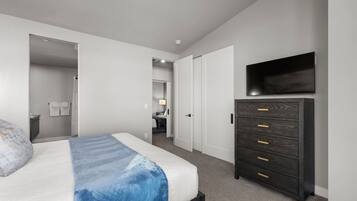 Een slaapkamer met een bed, een kaptafel, een televisie en een badkamer die door een open deur zichtbaar is.