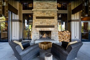 An outdoor seating area with stone fireplace, wicker furniture, and a stack of firewood.
