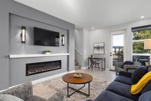 A modern living room with a fireplace, a flat-screen TV, and a dining area with a table and chairs.
