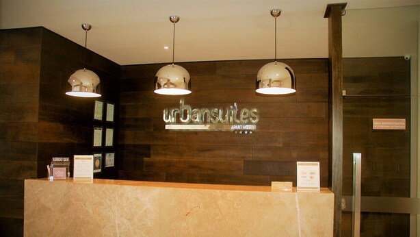 A reception desk with a sign reading "Urban Suites" and three pendant lights above it. - Urban Suites (Santa Cruz)