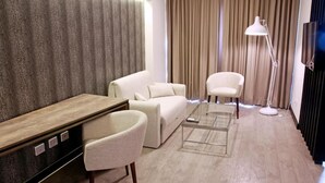 A modern living room with a sofa, armchair, coffee table, and a desk with a lamp. - Urban Suites (Santa Cruz)