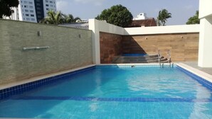 A swimming pool with a tiled edge, a wooden wall, and a metal ladder leading into the pool. - Urban Suites (Santa Cruz)
