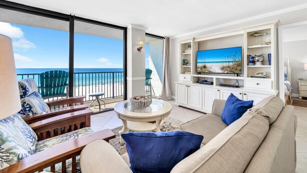 A spacious living room with a large window overlooking the beach, a comfortable sofa, a coffee table, and a TV.