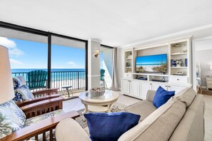 Un salon spacieux avec une grande fenêtre donnant sur la plage, un canapé confortable, une table basse et un téléviseur.