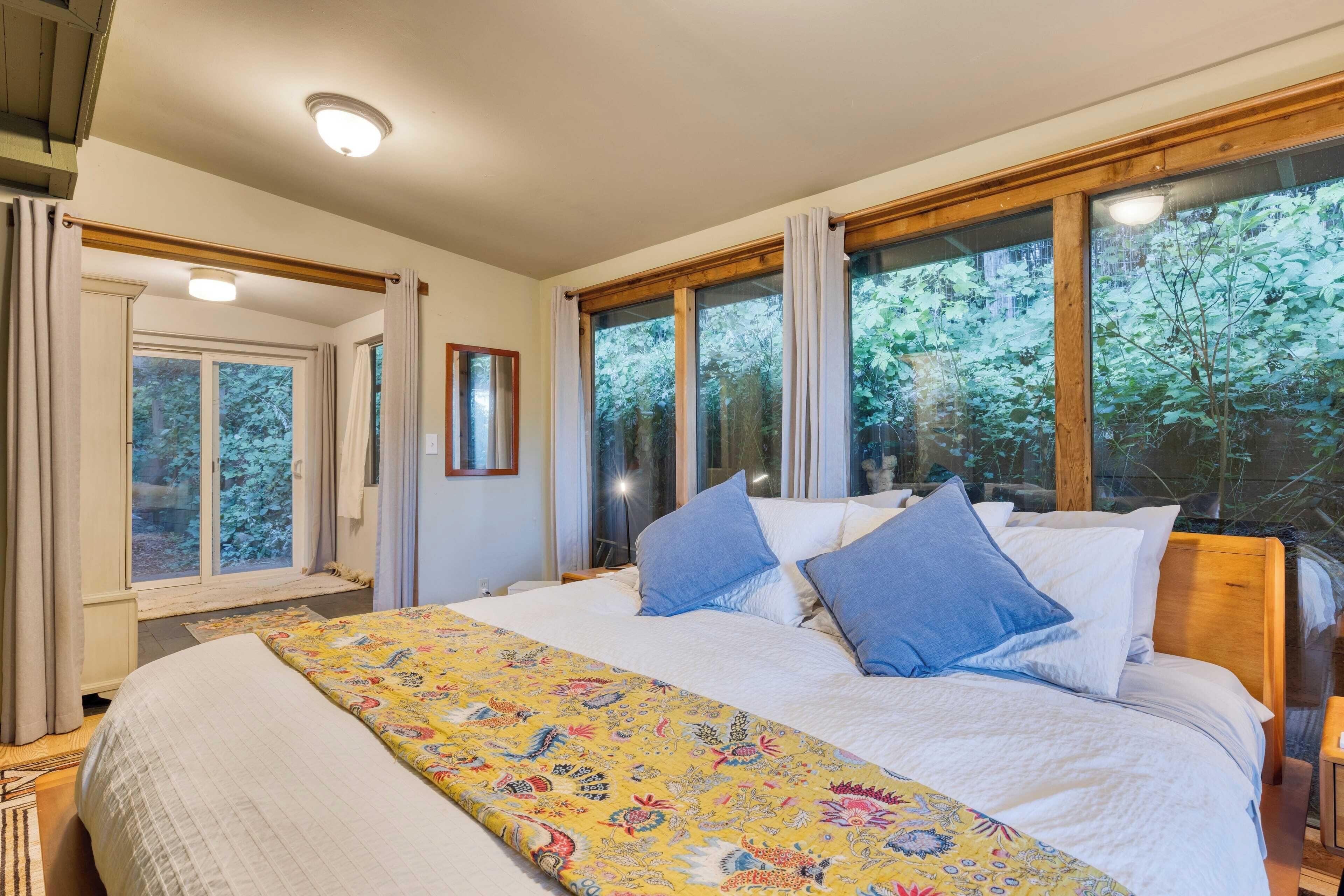 Een slaapkamer met een groot bed, meerdere ramen en uitzicht op bomen.