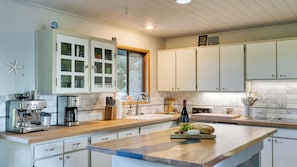 A modern kitchen with white cabinets, a coffee machine, and a wooden countertop. - Coastal Escape w/ Balcony, Firebowl & Ocean Views Near Manzanita Sunset House by Avantstay (Manzanita)