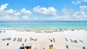 Une plage bordée de rangées de chaises longues et de parasols, avec une tour de surveillance et l’océan en toile de fond.