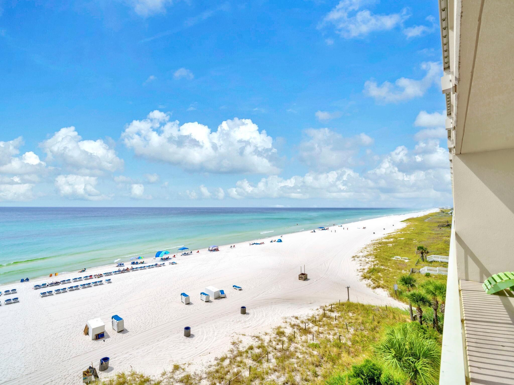 A beach with white sand, clear blue water, and a few beach umbrellas.