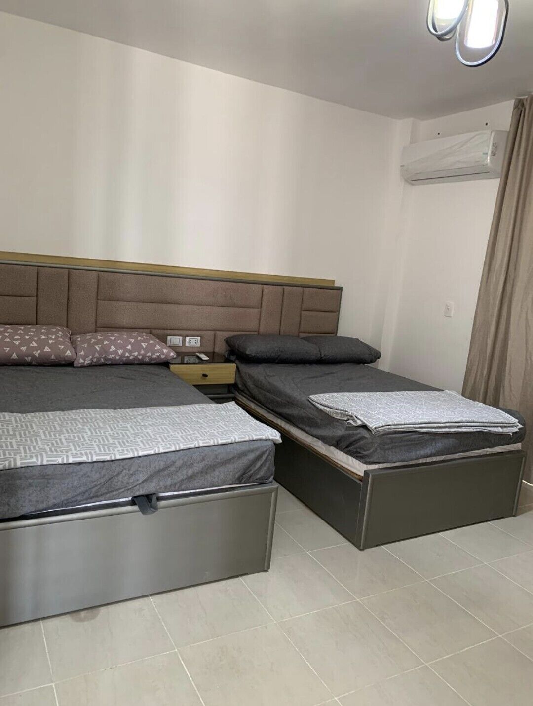 A bedroom with two beds, a nightstand, and an air conditioning unit.