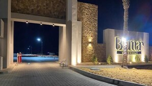 Entrada de un hotel con fachada de piedra, una palmera y un cartel que dice 'Bumar'.