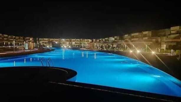 Vista nocturna de una piscina rodeada de edificios e iluminación.