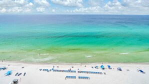 Una playa con filas de sillas azules y sombrillas, cielo azul despejado y agua turquesa.