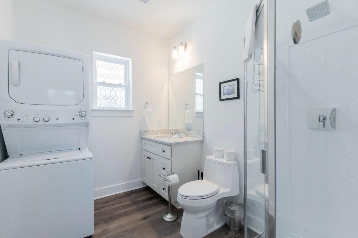 A modern bathroom with a built-in washer and dryer, a toilet, and a shower enclosure.