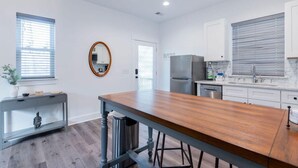 A modern kitchen with white cabinets, a stainless steel refrigerator, and a wooden dining table. - Charming Old Town Loft, Nestled in the Heart of Historic Bluffton, SC (Bluffton)
