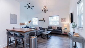 A modern living room with a dining area, grey sofas, a chandelier, and a ceiling fan. - Charming Old Town Loft, Nestled in the Heart of Historic Bluffton, SC (Bluffton)