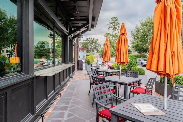 An outdoor seating area with tables and chairs, orange umbrellas, and a view of the street. - Charming Old Town Loft, Nestled in the Heart of Historic Bluffton, SC (Bluffton)