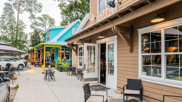 An outdoor seating area with tables and chairs, a building with a 'LOCAL' sign, and a blue storefront in the background. - Charming Old Town Loft, Nestled in the Heart of Historic Bluffton, SC (Bluffton)
