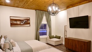 A bedroom with two beds, a TV, a wooden cabinet, and a painting on the wall. - Alterra:Slees 8,Steps to Main St,Serene (Madison)