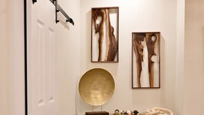 A hallway with a wooden ceiling, a white door, a wooden cabinet with decorative items, and two abstract paintings on the wall. - Alterra:Slees 8,Steps to Main St,Serene (Madison)