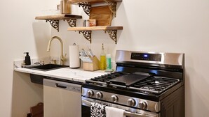 A compact kitchen with a stainless steel stove, oven, and dishwasher. There are wooden shelves above the sink and a wooden ceiling. - Alterra:Slees 8,Steps to Main St,Serene (Madison)