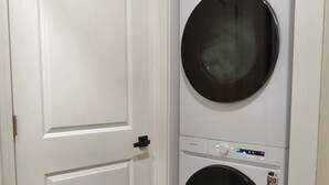 A laundry room with a white door and two stacked washing machines. - Alterra:Slees 8,Steps to Main St,Serene (Madison)