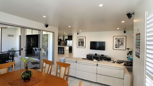 A modern living room with a sofa, TV, and artwork. There is a dining area with a table and chairs.