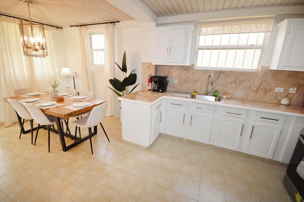 Une cuisine moderne avec des meubles blancs, un plan de travail en marbre et un coin repas comprenant une table et des chaises en bois.