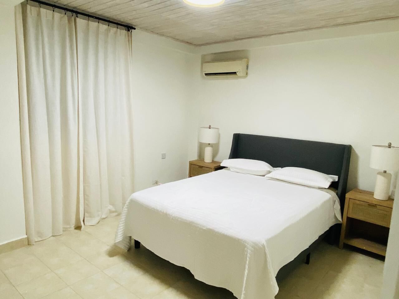 Ein Hotelzimmer mit einem Einzelbett, zwei Nachttischen mit Lampen, einem Deckenventilator und einer Klimaanlage.