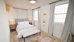 Une chambre à coucher avec un lit, des tables de chevet, un banc, un tapis et une fenêtre avec des rideaux.