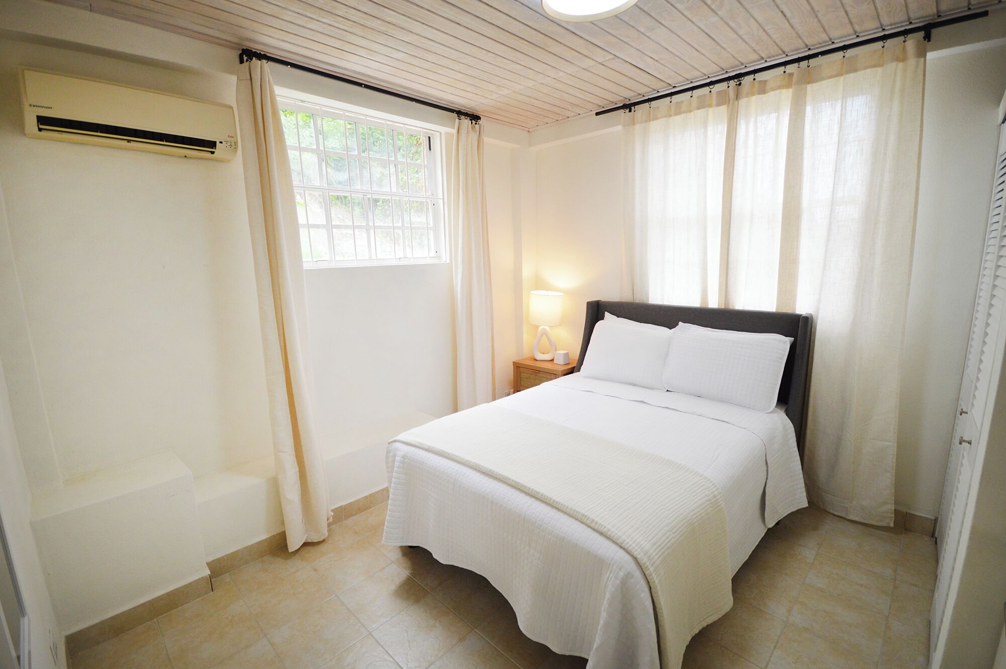 Un dormitorio con cama, mesita de noche, lámpara y ventana con cortinas.
