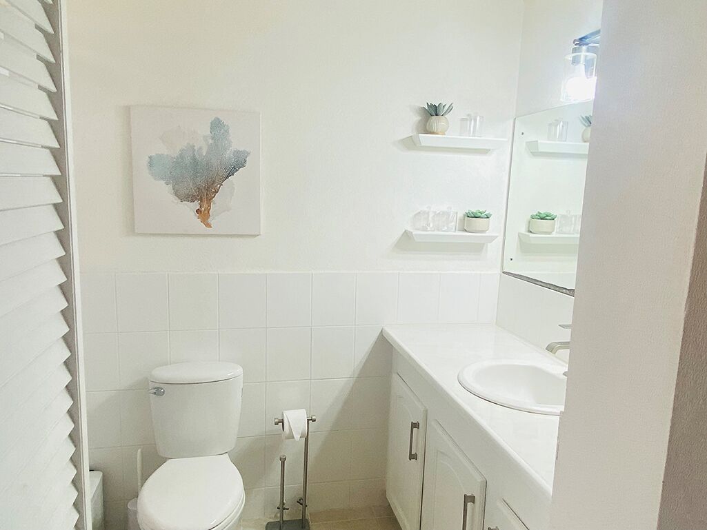 A bathroom with a toilet, sink, and shelves with toiletries.