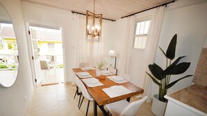 Un coin repas avec une table en bois dressée pour quatre personnes, des chaises blanches, un luminaire suspendu et une plante en pot.