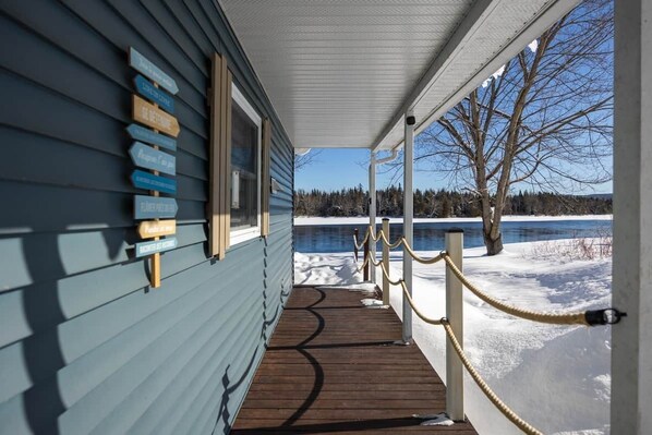 A wooden deck leading to a building with a view of a frozen lake and trees. - Chalet Entre Lac et Rivière (Weedon)