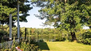 En fredfyldt have ved søen med et træværkhegn, frodig vegetation og krystalklart vand.