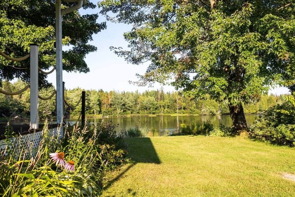Un jardin paisible au bord du lac, agrémenté d’une clôture en bois, d’une végétation luxuriante et offrant une vue dégagée sur le lac.