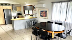 A modern kitchen with a central island, a dining area with a round table and chairs, and a large window with curtains. - Central Park - Rainbow Beach (Rainbow Beach)