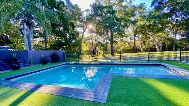 A rectangular swimming pool with a wooden deck, surrounded by well-maintained grass and a fence. - Central Park - Rainbow Beach (Rainbow Beach)