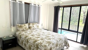 A bedroom with a bed, a nightstand, a lamp, and a window with curtains. - Central Park - Rainbow Beach (Rainbow Beach)