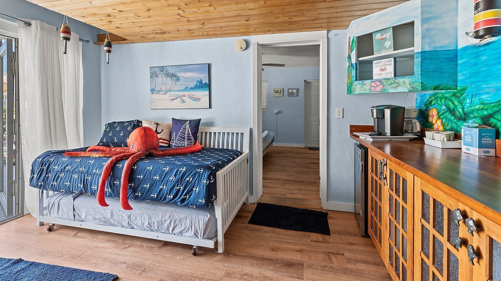Une chambre avec un lit, un plafond en bois, un tableau, un coin cuisine avec un comptoir et des appareils électroménagers, et une vue sur la pièce adjacente.